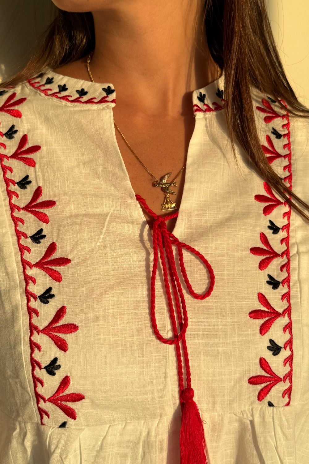 Vestido blanco de manga larga con bordados rojos en las mangas y el pecho. Un elegante pompón rojo en el centro del pecho añade un toque único y vibrante.