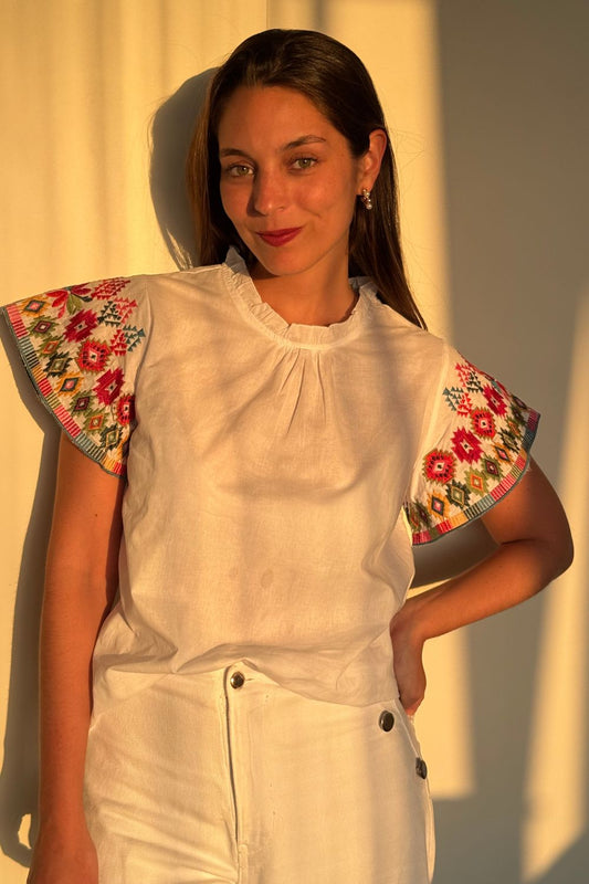 Blusa blanca con mangas completamente bordadas en una mezcla vibrante de colores.
Un diseño único y lleno de energía, perfecto para darle un toque colorido a tu look.