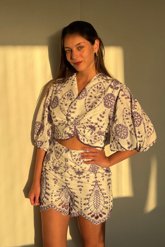 Blusa 3/4 blanca con bordado en todo su diseño. Detalles de flores lilas en la parte inferior y mangas abuchonadas que aportan un toque elegante y femenino. Ideal para cualquier ocasión especial.