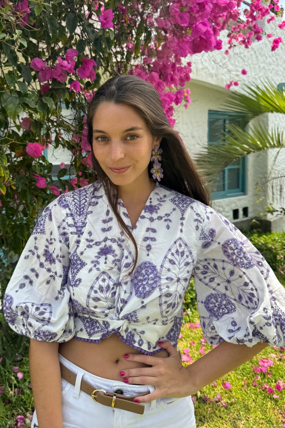 Blusa 3/4 blanca con bordado en todo su diseño. Detalles de flores lilas en la parte inferior y mangas abuchonadas que aportan un toque elegante y femenino. Ideal para cualquier ocasión especial.