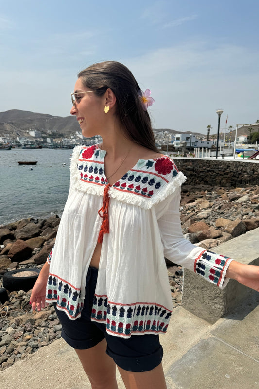 Blusa de manga larga con bordado de flores rojas, azules y celestes en el pecho, las mangas y la espalda. Un encantador pompón en el centro del pecho le da un toque especial y único.