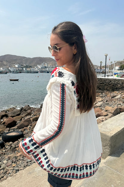 Blusa de manga larga con bordado de flores rojas, azules y celestes en el pecho, las mangas y la espalda. Un encantador pompón en el centro del pecho le da un toque especial y único.