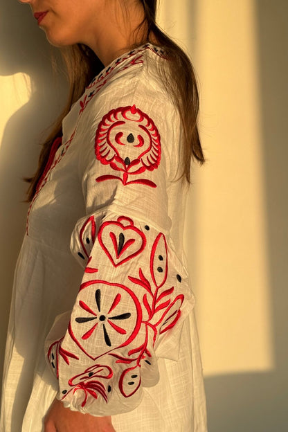 Vestido blanco de manga larga con bordados rojos en las mangas y el pecho. Un elegante pompón rojo en el centro del pecho añade un toque único y vibrante.